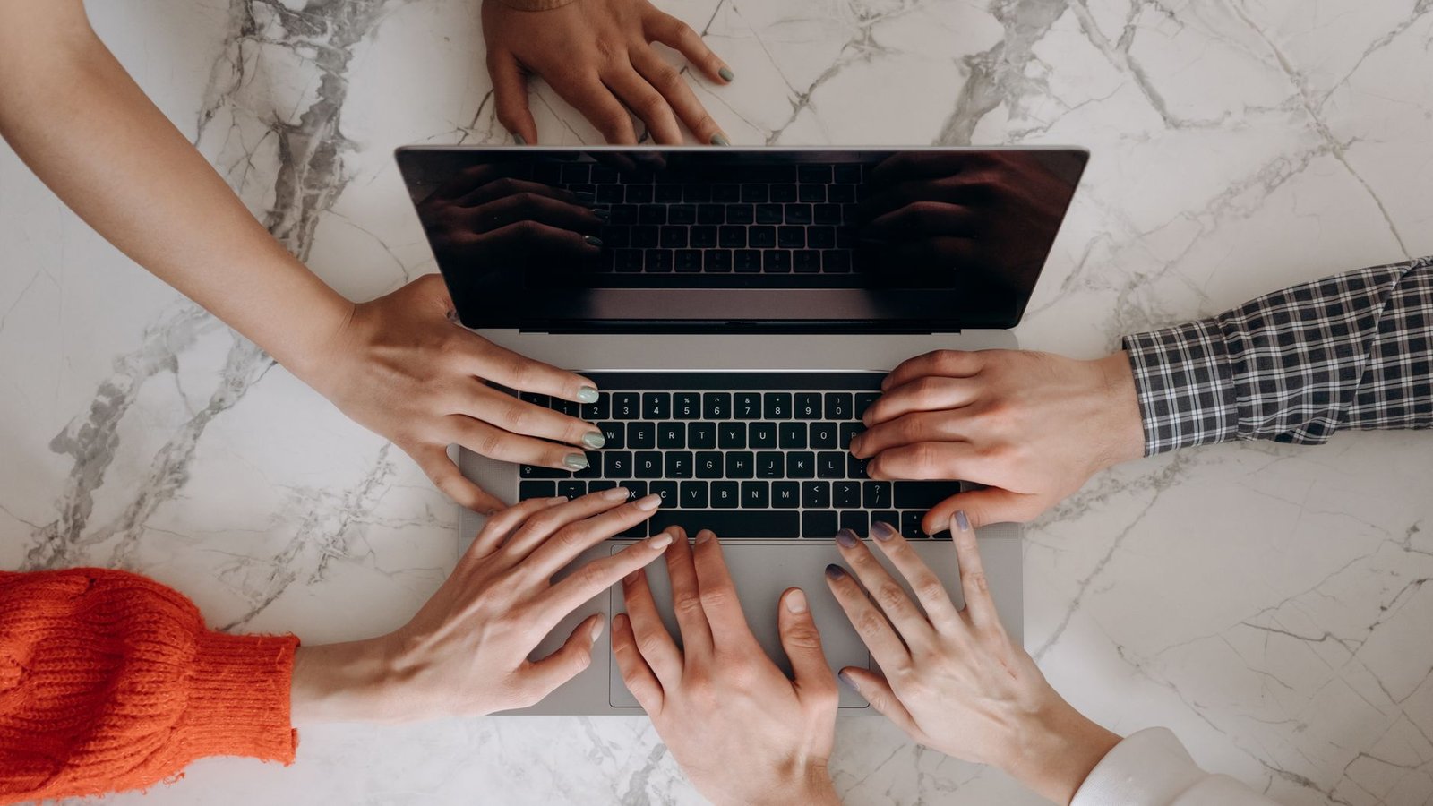 Top view of multiple hands working together on a laptop keyboard, symbolizing teamwork. — Challenges to Overcome