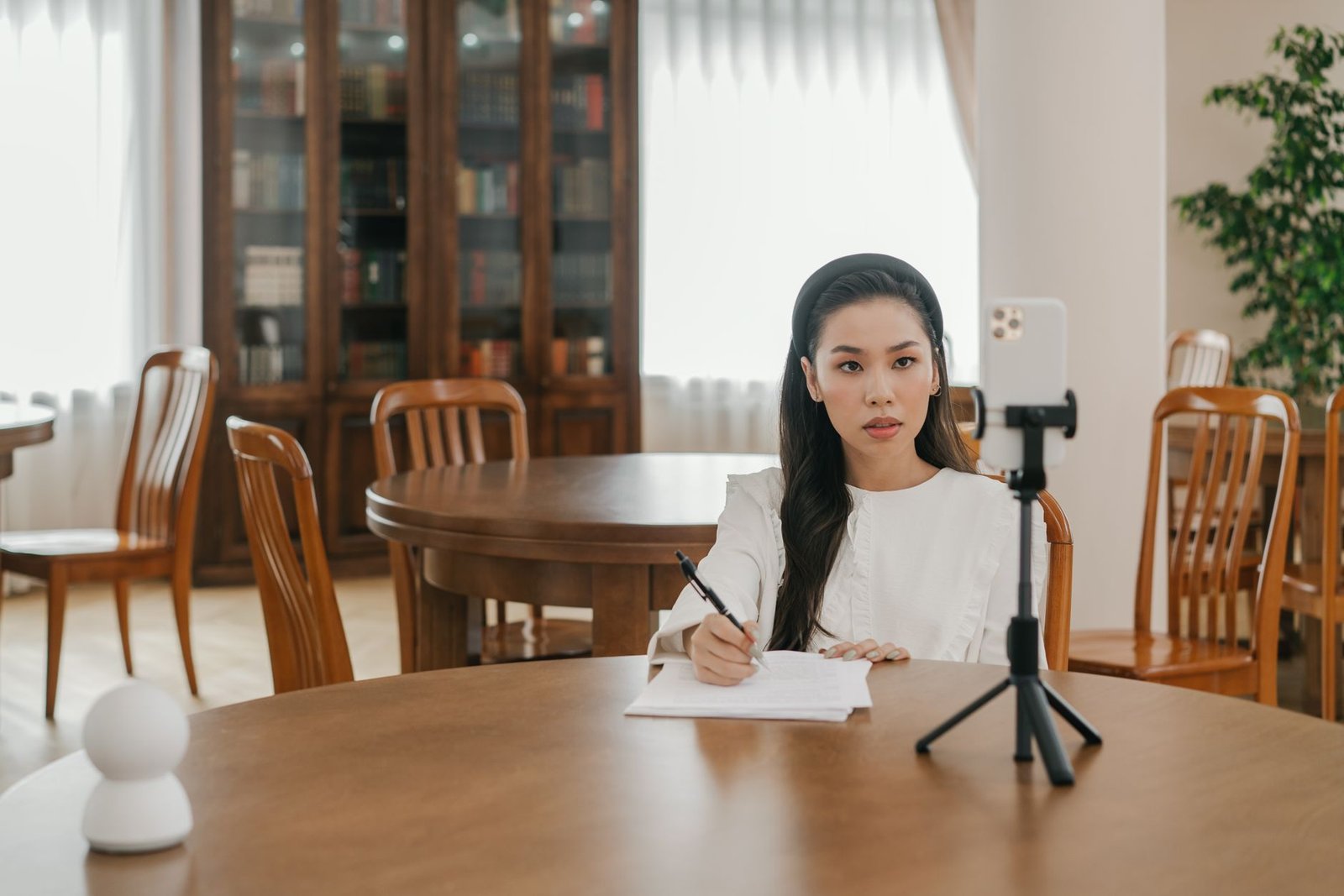 Young Asian woman vlogging in a cozy home office setup using a smartphone and tripod. — Coin game crypto casino
